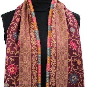 Op de afbeelding: Een bordeauxrode sjaal met een bloemenpatroon en gouden, roze en blauwe bies. De sjaal is over een zwart manekin gedrapeerd.