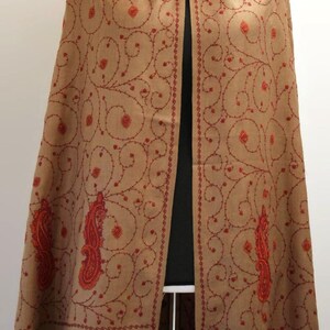 May include: A brown shawl with red embroidery featuring a paisley design. The shawl is draped over a mannequin.