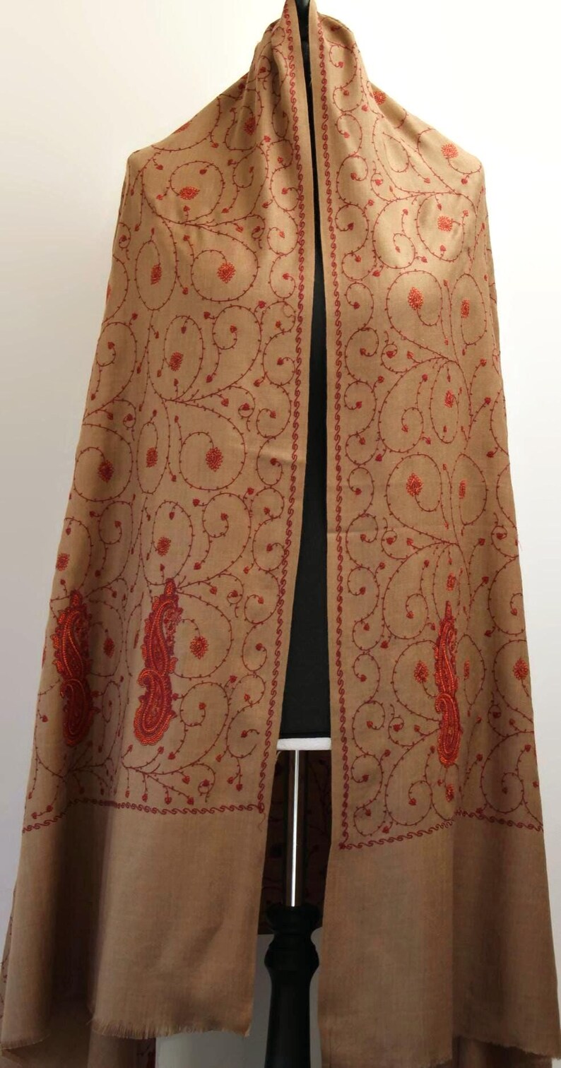 May include: A brown shawl with red embroidery featuring a paisley design. The shawl is draped over a mannequin.