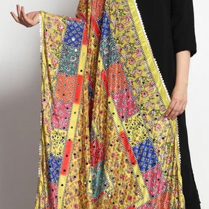 May include: A yellow silk dupatta with a patchwork design featuring colorful squares and floral patterns. The dupatta has a white border with small pearl-like embellishments and is adorned with small round mirrors.