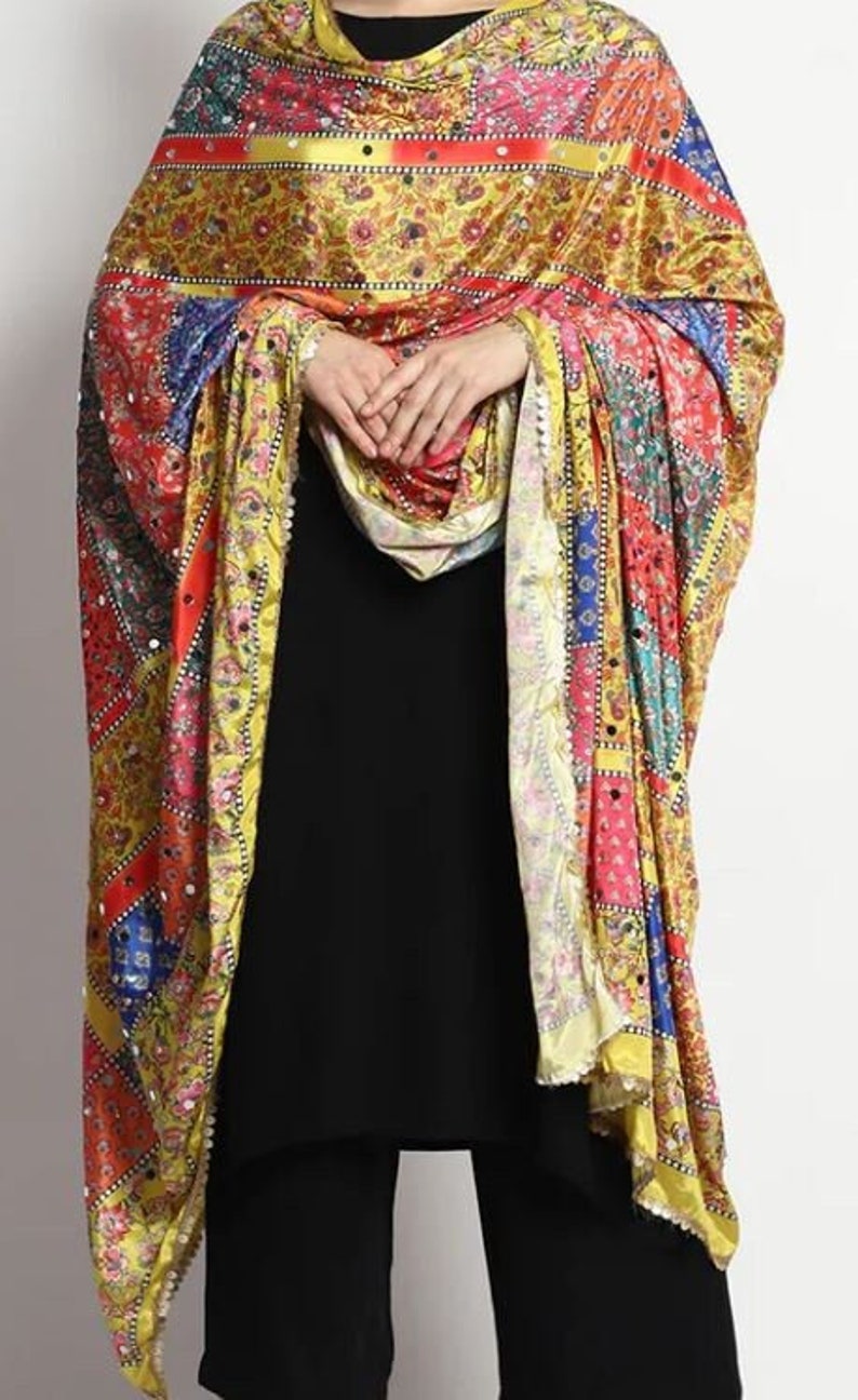 May include: A yellow, red, blue, and green patterned silk scarf with a beaded border. The scarf is draped over a person's shoulders.
