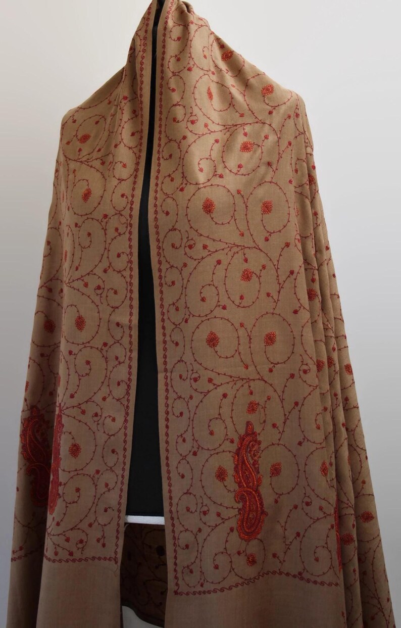 May include: A brown shawl with red embroidery in a paisley pattern. The shawl is made of wool and has a soft, luxurious feel.