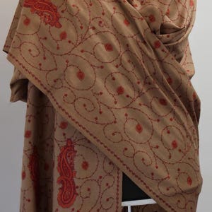 May include: A brown shawl with red embroidery featuring a paisley design and floral patterns.