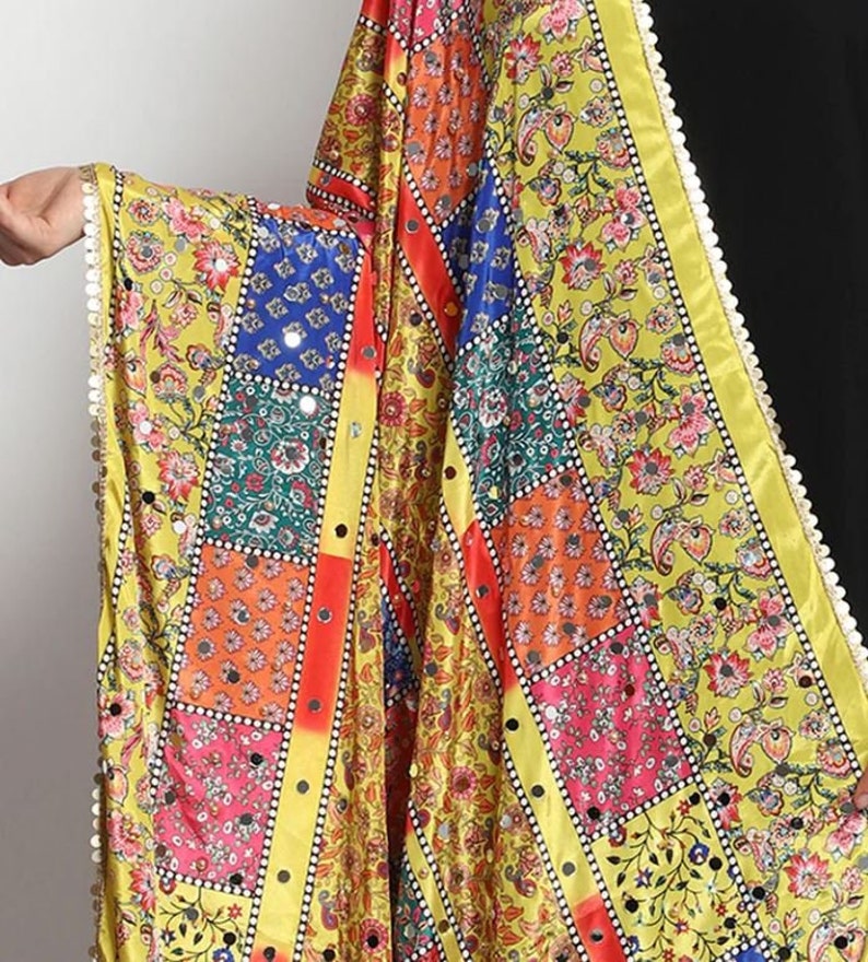 May include: A colorful patchwork dupatta with a yellow base and floral patterns. The dupatta has a gold trim and is decorated with small mirrors.