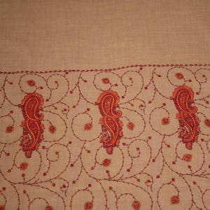 May include: A beige shawl with a red embroidered border featuring paisley patterns.
