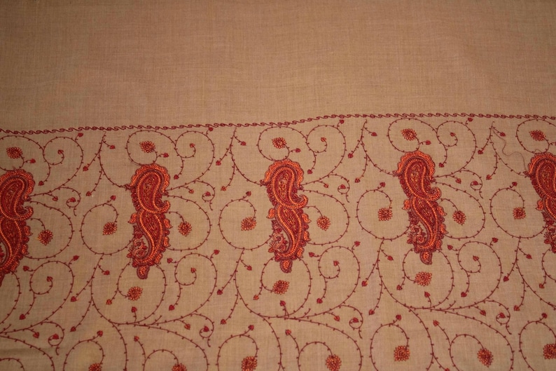 May include: A beige shawl with a red embroidered border featuring paisley patterns.