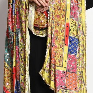 May include: A yellow, pink, blue, and green patterned silk scarf with a beaded trim. The scarf has a patchwork design with floral motifs and mirror embellishments.