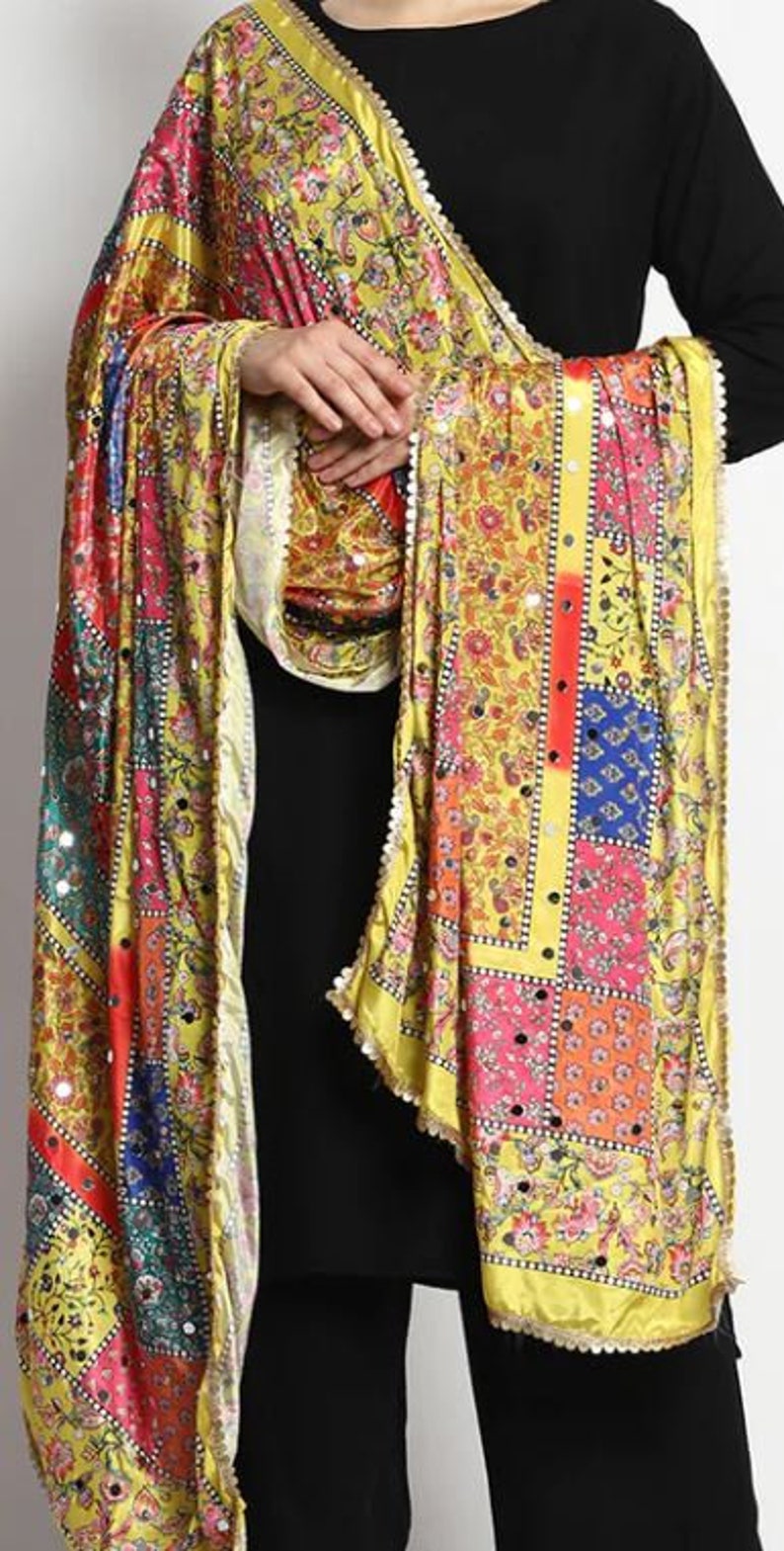 May include: A yellow, pink, blue, and green patterned silk scarf with a beaded trim. The scarf has a patchwork design with floral motifs and mirror embellishments.