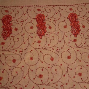 May include: A beige shawl with a delicate red embroidered pattern of paisley shapes and swirling vines.