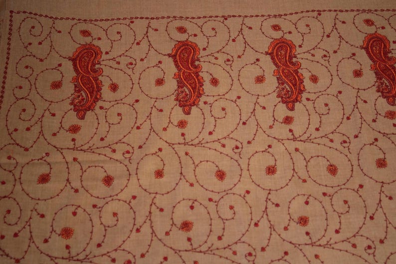 May include: A beige shawl with a delicate red embroidered pattern of paisley shapes and swirling vines.