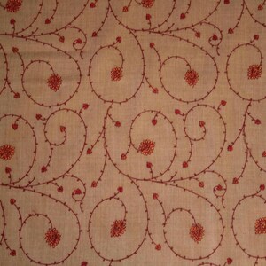 May include: A beige fabric with a repeating pattern of red embroidered floral designs. The design features swirling vines with small red flowers.