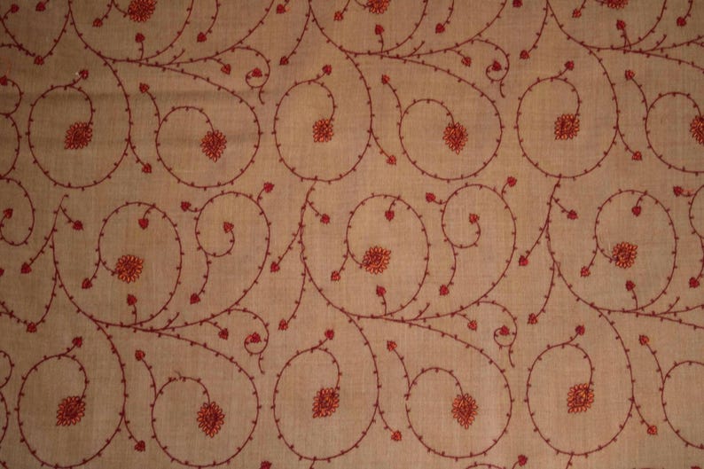 May include: A beige fabric with a repeating pattern of red embroidered floral designs. The design features swirling vines with small red flowers.