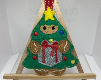 May include: A green felt Christmas tree ornament with gingerbread details, a red bow, and a silver glitter present. The tree has a yellow star on top and is decorated with red and blue ornaments.