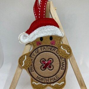 May include: A gingerbread man Christmas ornament with a red hat and a button that says "Property of Father Christmas North Pole".