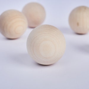 Op de afbeelding: Vier gladde, ronde houten ballen op een witte achtergrond. De ballen zijn allemaal even groot en gemaakt van licht hout.