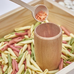 transfer of rice with a wooden spoon from a wooden cup to a wooden sensory tray.