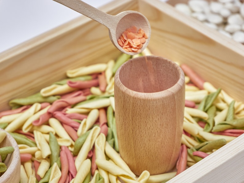 transfer of rice with a wooden spoon from a wooden cup to a wooden sensory tray.