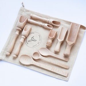 Könnte beinhalten: Ein Set aus Holzschöpfen und -löffeln in einem natürlichen Leinenbeutel. Die Schaufeln sind in verschiedenen Größen und Formen erhältlich, perfekt zum Schaufeln von Sand, Reis oder anderen kleinen Gegenständen. Die Tasche hat ein Logo mit der Aufschrift "Wooden Freedom by Nature Toys".