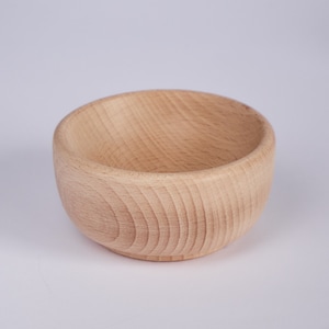 Puede incluir: Un pequeño cuenco de madera redondo con un acabado de madera natural. El cuenco está vacío y tiene una superficie lisa ligeramente texturizada.