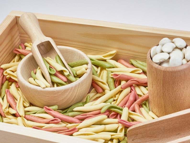 wooden tray filled with beans and pasta with wooden bowl inside, wooden scoops and wooden cup.