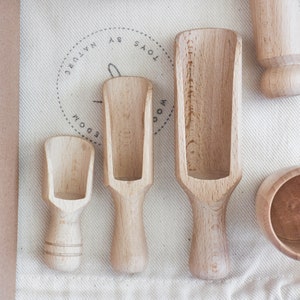 Three scoops of different sizes, wooden cup and pin lying on a cotton sack.