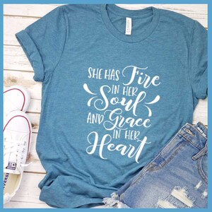 May include: A teal blue t-shirt with the text "She has Fire in her Soul and Grace in her Heart" printed in white.
