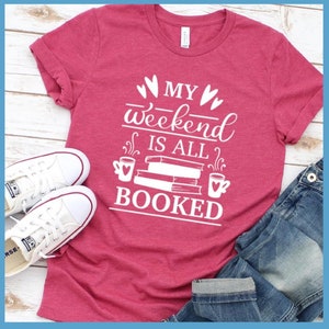 May include: A red t-shirt with white text that reads "My weekend is all booked" with a stack of books and coffee cups on either side.