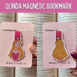 May include: Pink magnetic bookmark featuring a princess illustration. The bookmark has a pink card with a slit to hold the bookmark in place. The princess has long blonde hair and is wearing a pink dress. The text "GLINDA MAGNETIC BOOKMARK" is at the top.