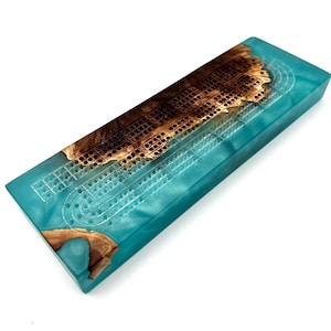 May include: A turquoise blue cribbage board with a brown wood inlay. The board is made of resin and has a unique, natural look.