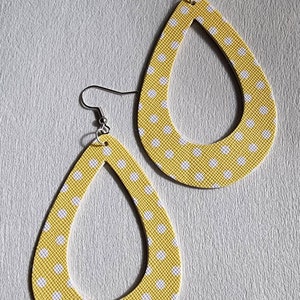 May include: A pair of teardrop-shaped earrings. The earrings are yellow with a white polka dot pattern. The earrings have a textured surface and are suspended from silver-colored fish hook ear wires.