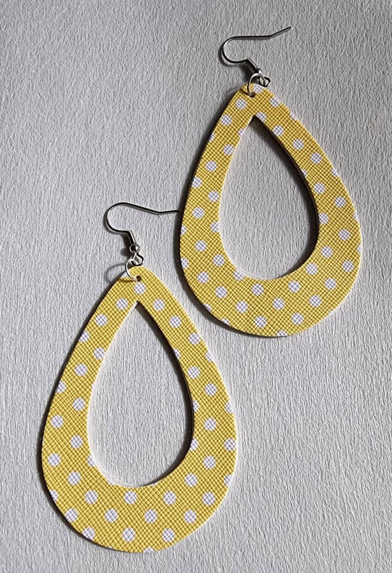 May include: A pair of teardrop-shaped earrings. The earrings are yellow with a white polka dot pattern. The earrings have a textured surface and are suspended from silver-colored fish hook ear wires.