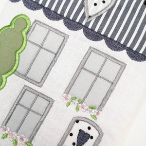 May include: A white embroidered house with a grey and white striped roof, a green bush, a grey door with black polka dots, and two windows with grey frames.