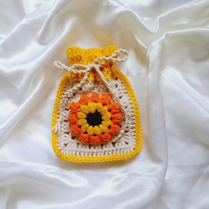 Op de afbeelding: Een gehaakte gele, oranje en cr&egrave;mekleurige tas in de vorm van een bloem met een trekkoord.