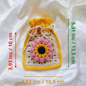 Op de afbeelding: Een gehaakte trekkoordtas met een geel, beige en roze bloemetjesontwerp. De tas meet 10 cm bij 10,5 cm en is 13,5 cm hoog.