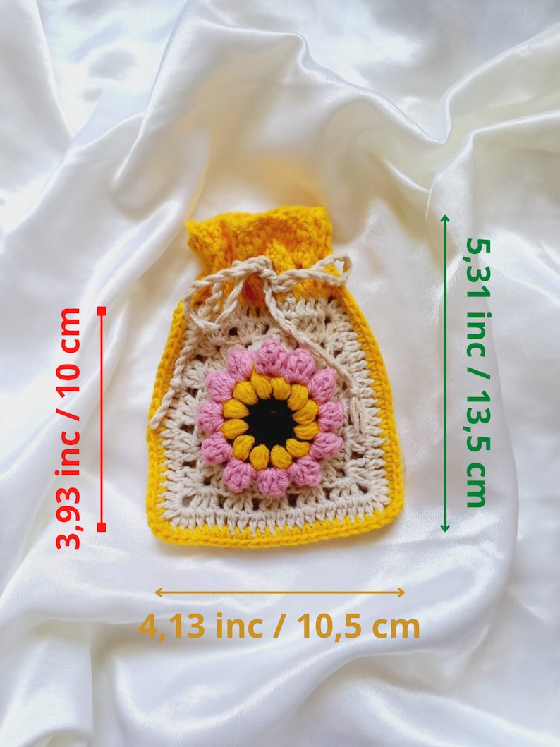 Op de afbeelding: Een gehaakte trekkoordtas met een geel, beige en roze bloemetjesontwerp. De tas meet 10 cm bij 10,5 cm en is 13,5 cm hoog.