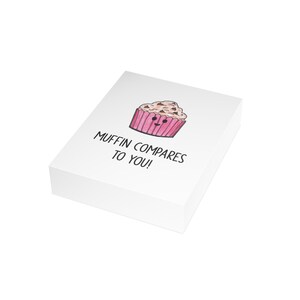 May include: White card with a pink and brown cartoon muffin with a smiling face. The text on the card reads "Muffin compares to you!"