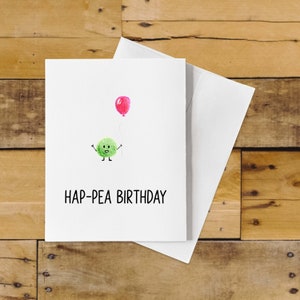 May include: A white card with a green pea cartoon holding a pink balloon. The text "HAP-PEA BIRTHDAY" is printed in black.