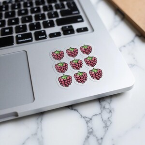 May include: Nine pink raspberry stickers on a silver laptop. The stickers are arranged in a 3x3 grid.
