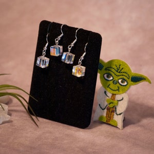May include: Four pairs of silver dangle earrings with clear iridescent cube-shaped crystals. The earrings are displayed on a black velvet jewelry stand.