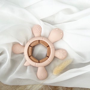 May include: A pink silicone baby teether shaped like a turtle with a wooden center. The teether has textured bumps and a ring for easy gripping.
