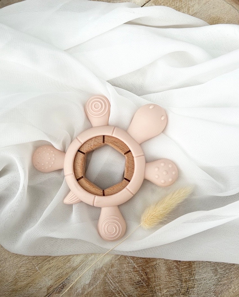 May include: A pink silicone baby teether shaped like a turtle with a wooden center. The teether has textured bumps and a ring for easy gripping.