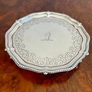 May include: A silver octagonal tray with a beaded edge and a decorative engraved design. The tray has four feet and a monogram in the center.