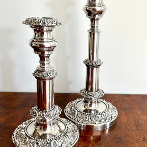 May include: A pair of silver candle holders with ornate designs. The candle holders have a round base and a tall, slender stem.