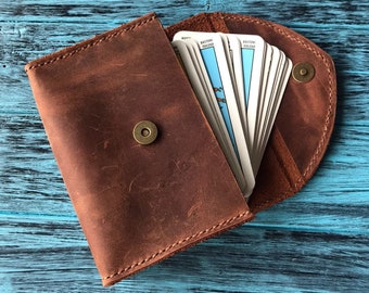 May include: A brown leather wallet with a flap closure and a snap button. The wallet is open and has a deck of playing cards inside.