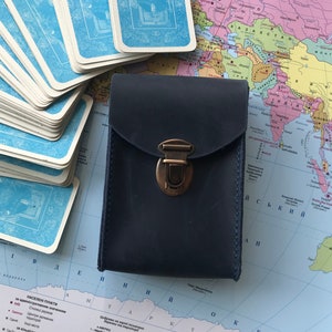 Può includere: Un portafoglio in pelle blu scuro con una chiusura in ottone e dettagli di cucitura. Il portafoglio è appoggiato su una mappa del mondo.