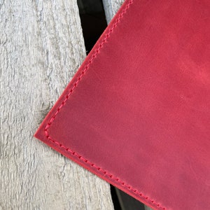 May include: A close-up of a red leather surface with red stitching around the edges. The leather has a slightly textured appearance.
