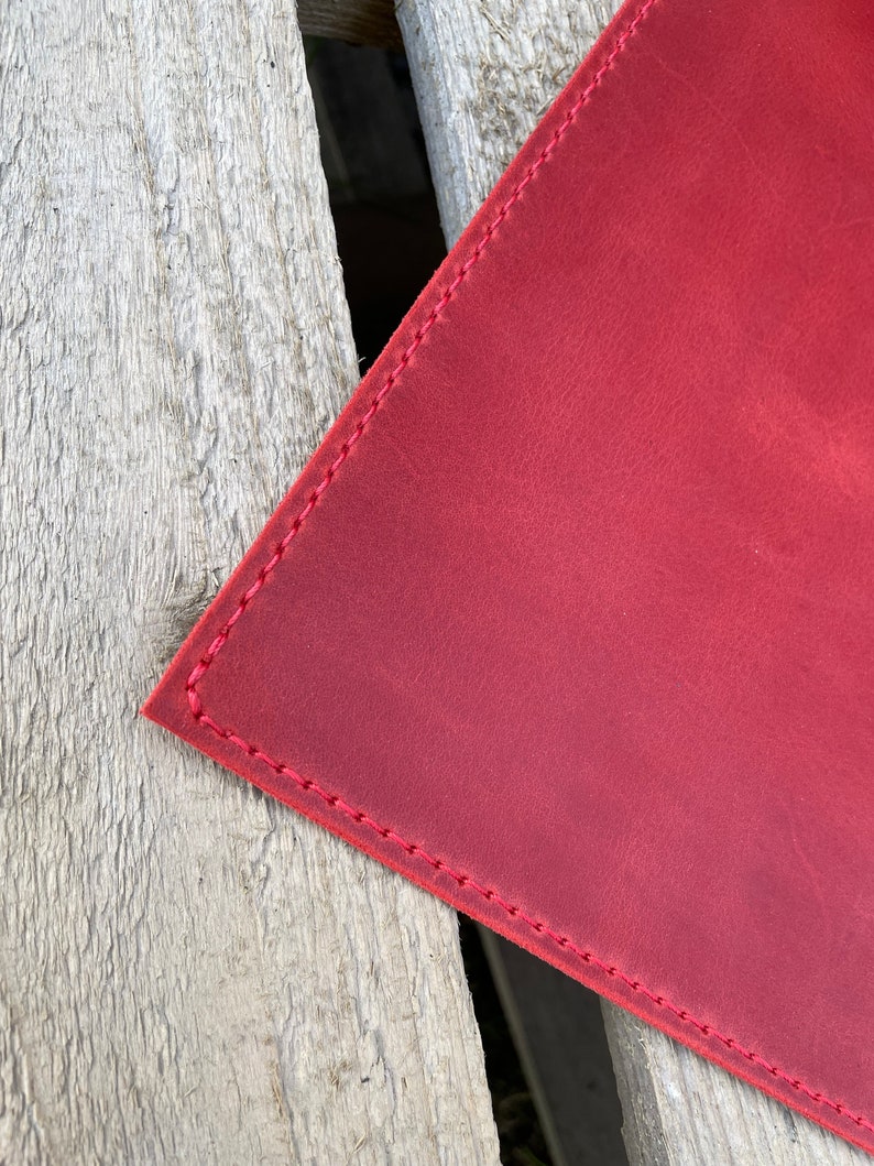 May include: A close-up of a red leather surface with red stitching around the edges. The leather has a slightly textured appearance.