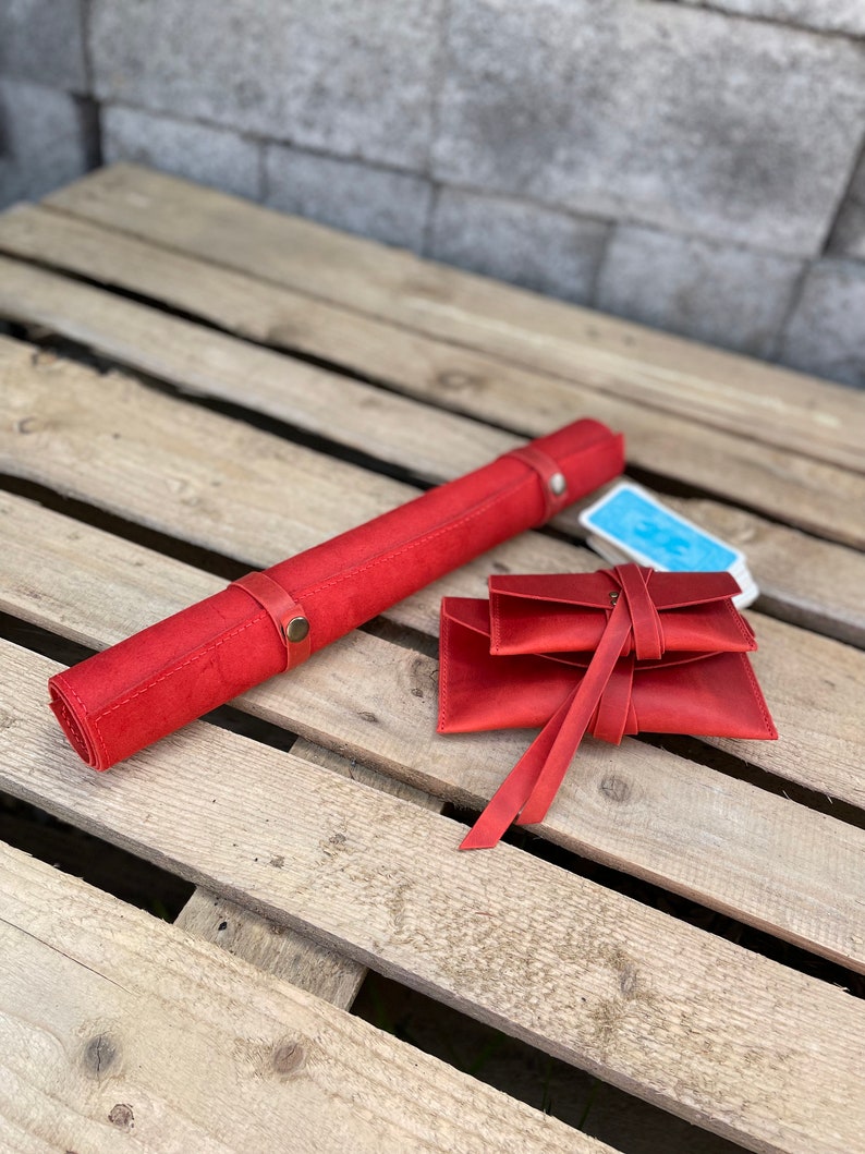 May include: Red leather roll-up game mat with a red leather pouch and a deck of cards. The mat and pouch have decorative stitching and metal accents.
