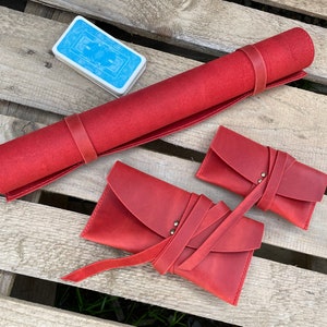May include: Three red leather pouches with a strap closure. The pouches are rolled up and tied with a strap. The pouches are on a wooden surface.