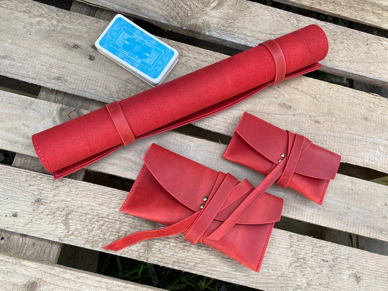 May include: Three red leather pouches with a strap closure. The pouches are rolled up and tied with a strap. The pouches are on a wooden surface.
